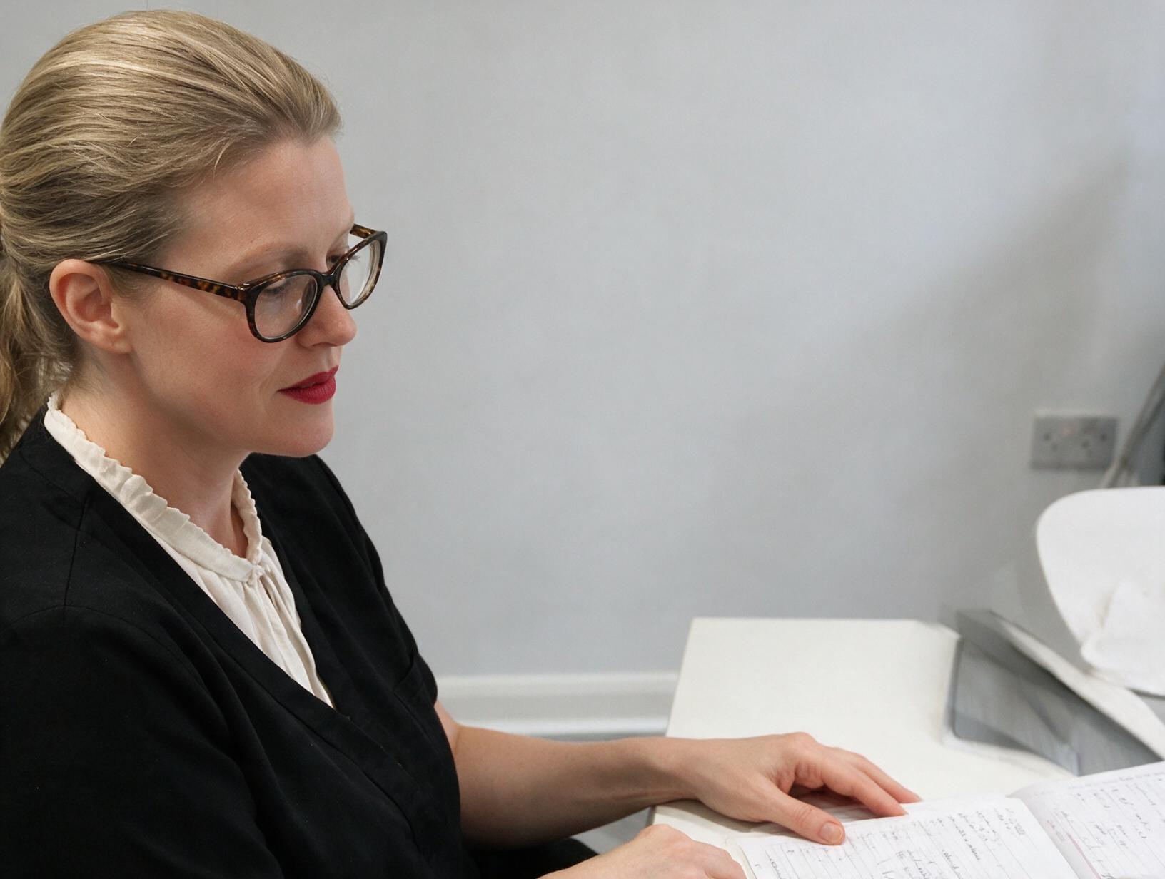 Woman with blonde hair tied back and tortoiseshell glasses, in black top and cream blouse